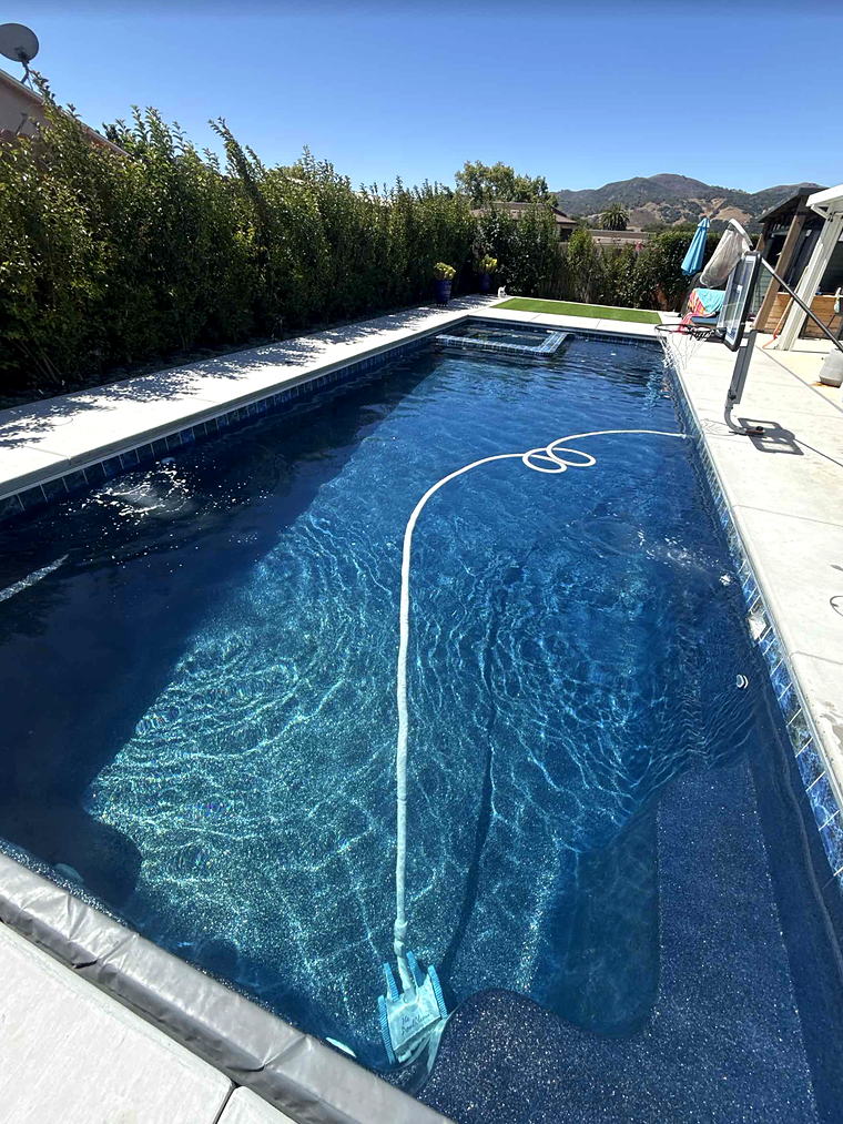 Completed Latham Astoria 16 fiberglass pool, forty feet long with deep blue water and an integrated spa at the far end, hills beyond the hedge