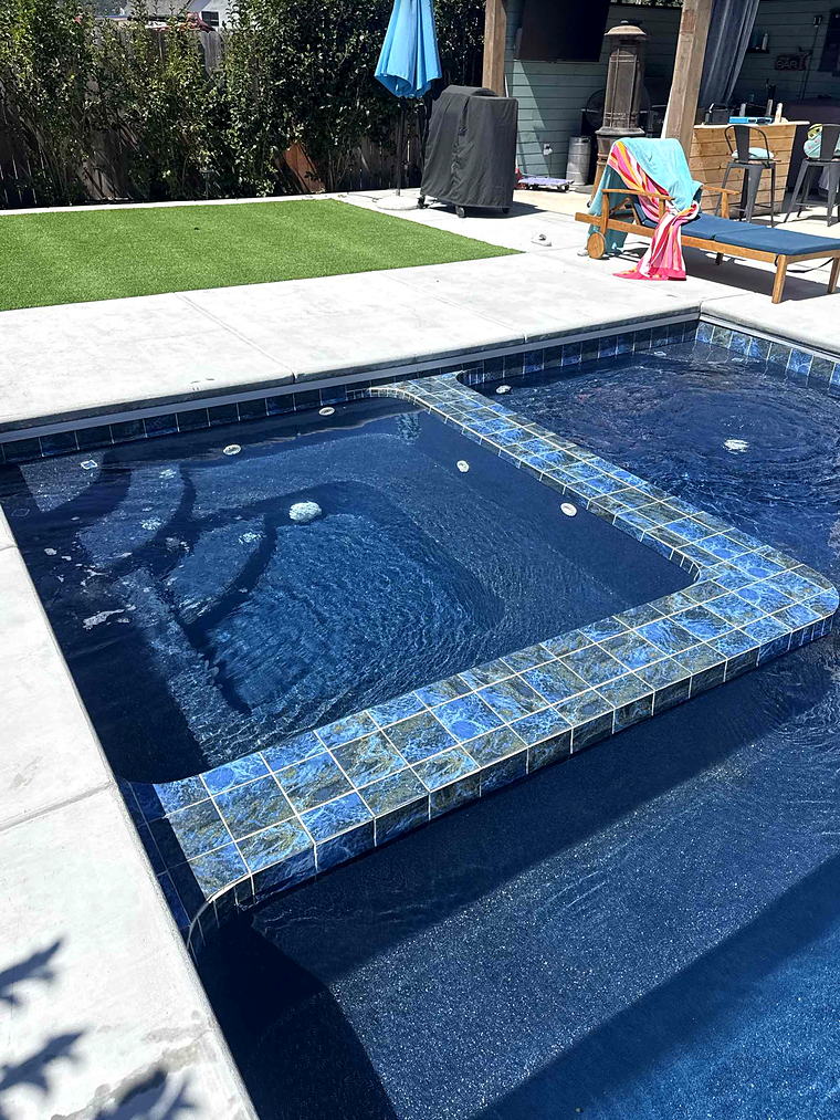 Spa and tanning ledge of a Latham Astoria 16 with an artificial turf lawn, outdoor bar and covered patio behind