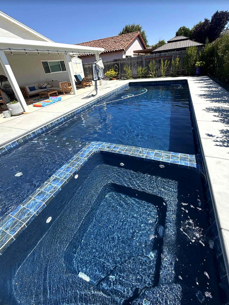 Integrated spa with a glass-tile raised dam wall spilling into the main pool of a Latham Astoria 16, covered patio behind